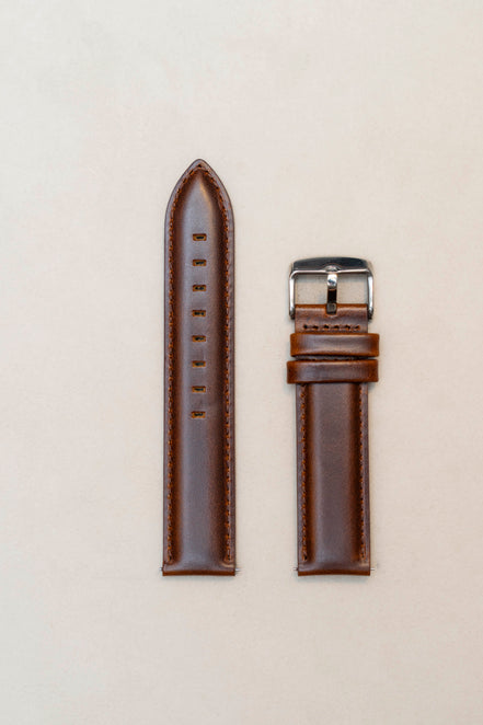 Brown leather watch strap with silver buckle on a beige background