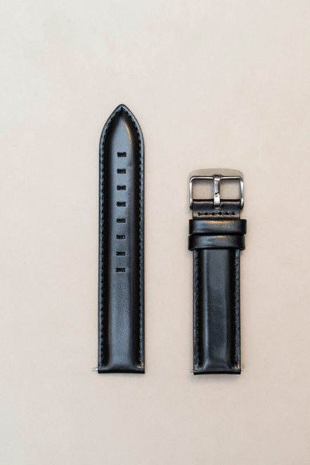 Black leather watch strap on a light beige background