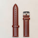 Brown leather watch strap with silver buckle on a light beige background