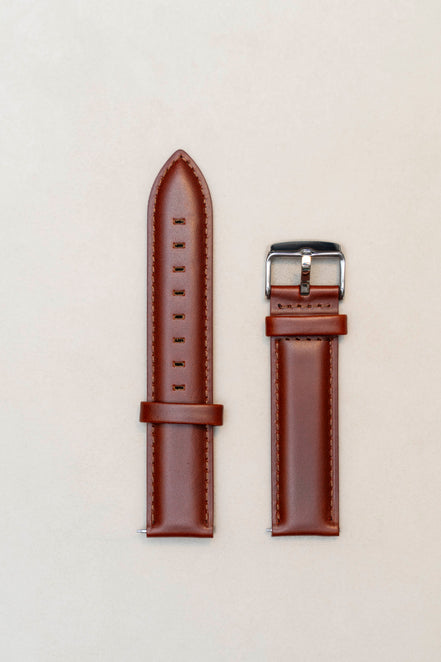 Brown leather watch strap with silver buckle on a light beige background